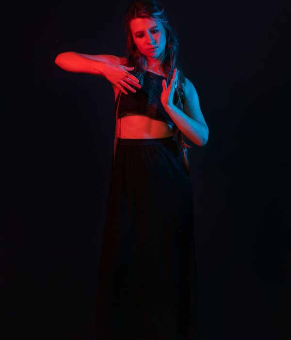 Woman performing a gentle back-stretching yoga pose in a dark room.